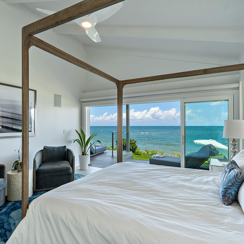 A serene bedroom featuring a bed, ocean view, and a single sofa with a mini plant from Sea of Glass Hawaii.