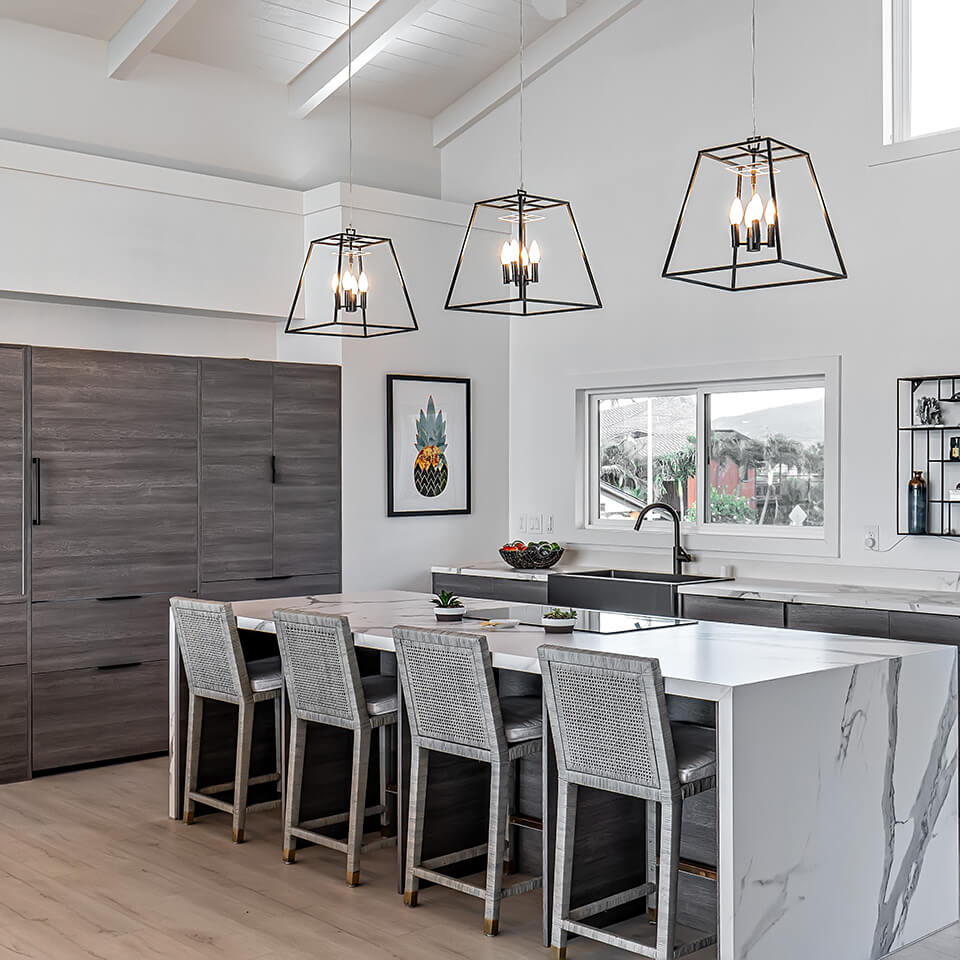 Stylish kitchen with white cabinets and a large island, complemented by a dining area with four chairs and a stunning bulleb  from Sea of Glass Hawaii.