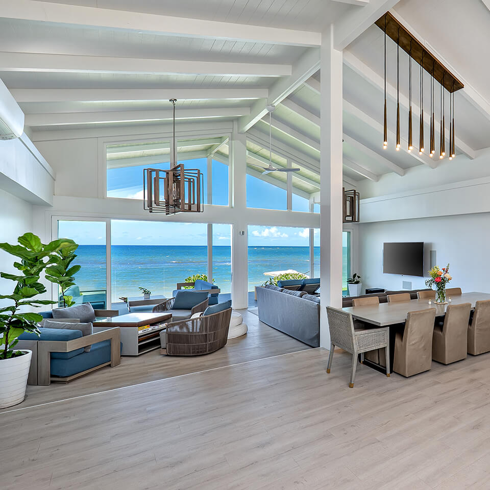 Spacious living room with an ocean view featuring a large dining table, chairs, TV, sofa, and plants, set in Sea of Glass Hawaii.