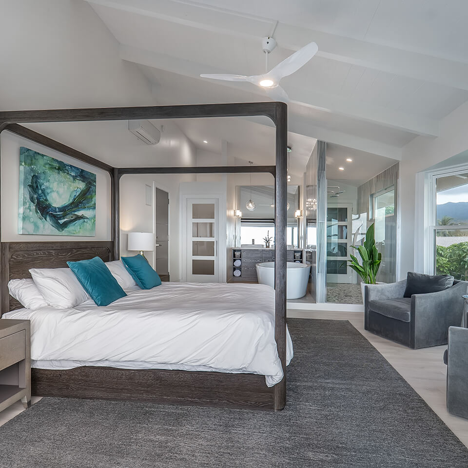 A luxurious bedroom featuring a four-poster bed, large painting, bathtub, sofa, and fan from Sea of Glass Hawaii.